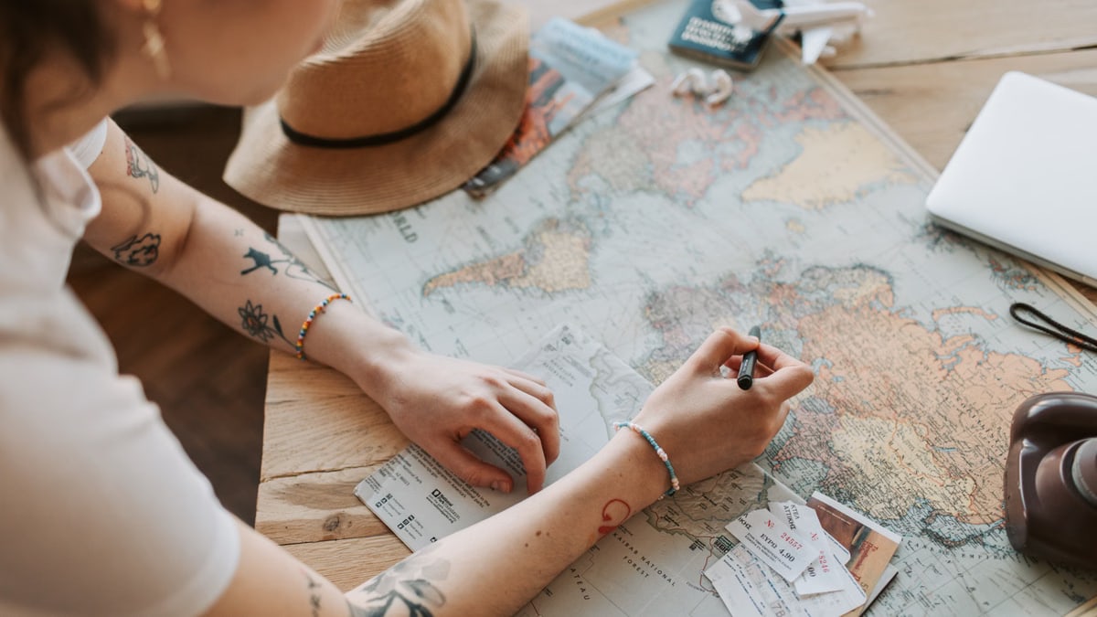Person planning a journey with a map, passport, and travel essentials on a wooden table.